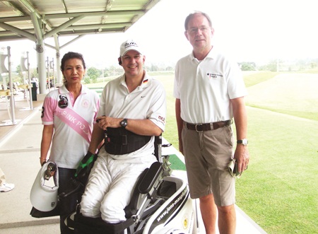 German Ambassador Dr. Hanns Schumacher, right, and Nittaya Patimasongkhro, left, the chairperson of YWCA and Special Olympics for disabled children, talk to Jens about his new golfing contraption. 