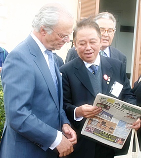Sutham Phanthusak, commissioner of the National Scout Organization of Thailand, shows King Carl VI Gustav of Sweden our front page when we featured him visiting their Majesties the King and Queen of Thailand to say thank you for help for the tsunami victims.  The man in the background is the chairman of the World Scout Foundation, Dr. Eberhard Von Koerber.  The pic was taken at a Scout camp outside Rome April 22, 2005.
