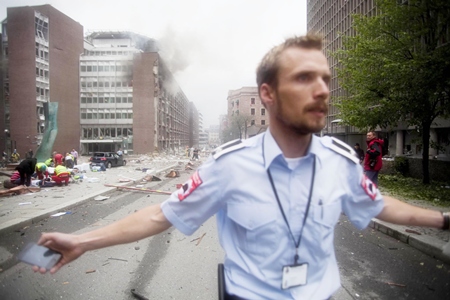 An official attempts to clear away spectators from buildings in the center of Oslo following an explosion that tore open several buildings including the prime minister’s office, shattering windows and covering the street with documents. (AP Photo/Fartein Rudjord)