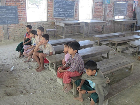 Barefoot children sit on old wooden benches, their toes making lines in the dirt floor.