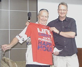 Open Forum host John Lyneham, a PCEC old timer just back in town for a short time, shows off a gift of a T-shirt to Hawaii Bob which could be a Pattaya motto; ‘Life, Liberty and the pursuit of Happy Hour’.