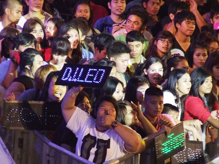 Spectators in front of stages holding electric signs cheer for their favorite musicians.