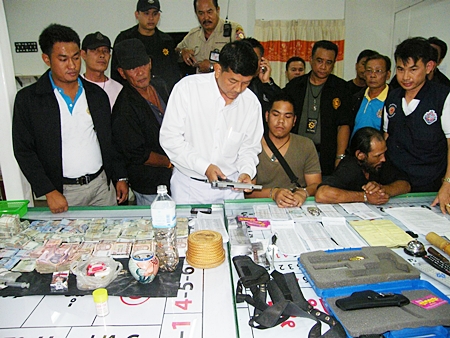 Banglamung District Chief Chawalit Saeng-Uthai inspects the confiscated handgun along with hundreds of thousands of baht, gambling slips and tables found during a raid on a Soi Buakaow home. 