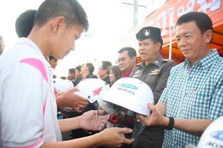 Banglamung District Chief Sakchai Taengho (right), along with Col. Col. Supachai Phuikaewkhum (2nd right) distribute motorcycle helmets to students.
