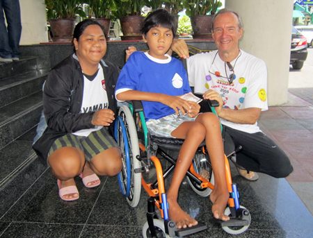 Lewis Underwood (right) presents a new wheelchair to Nathawat and his mother in front of Nongprue City Hall.