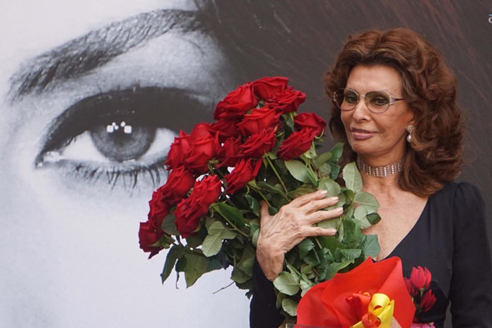 Sophia Loren holds a bunch of red roses as she stands in front a giant portrait of herself after being awarded with the honorary citizenship of Naples, Italy, Saturday, July 9. (Cesare Abbate/ANSA Via AP)
