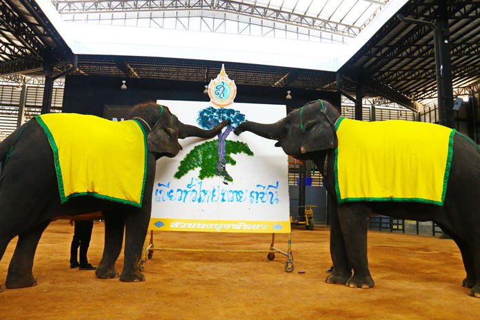 Two elephants write “green across Thailand to dedicate to HM the Queen” with their trunks.
