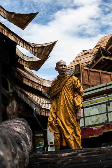 A monk from Sriworaram Temple looks over wood that survived a major fire at Baan Phayamai village. The wood has been donated to the temple to build a sala. (Photo by Tachai Nawapanit)
