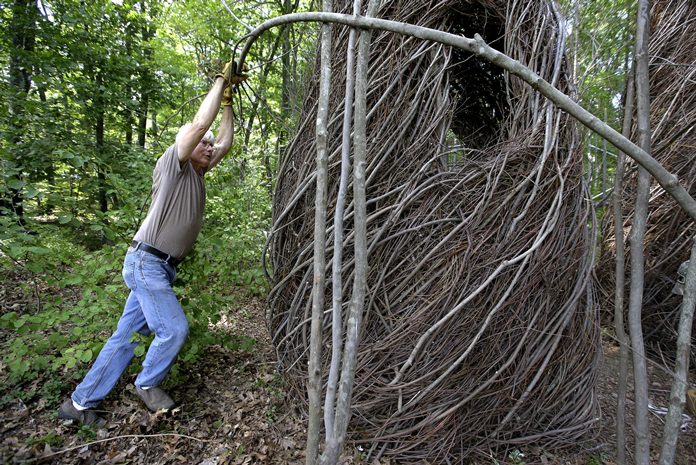 Sculptor Patrick Dougherty bends a sapling while constructing a sculptural installation “The Wild Rumpus,” from branches and sticks on the grounds of the Tower Hill Botanic Garden, in Boylston, Mass. (AP Photo/Steven Senne)