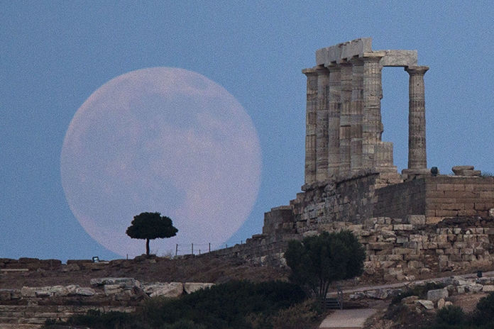 In this June 20, 2016 file photo, the full moon rises behind a tree next to the ruins of the ancient marble Temple of Poseidon, built in 444 BC, at Cape Sounion, southeast of Athens, on the eve of the summer solstice. A California-led research team reported that the moon formed within 60 million years of the birth of the solar system. (AP Photo/Petros Giannakouris)
