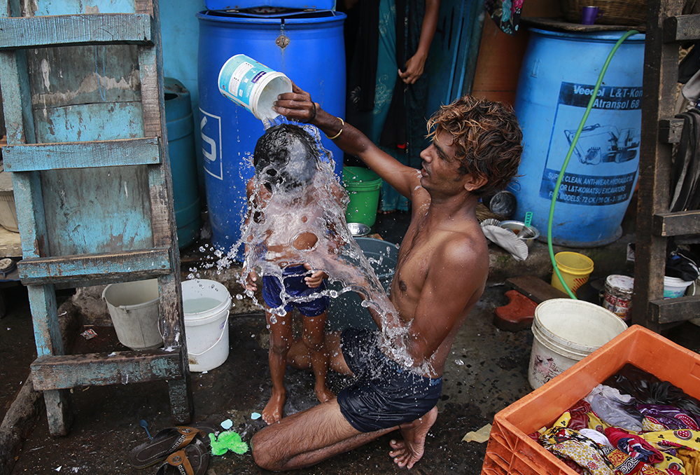 In this May 23, 2016, file photo, a man bathes his son on a hot afternoon in a slum in Mumbai, India. For the third straight year, Earth set a record for the hottest year, NOAA and NASA announced. NASA says 2016 was warmer than 2015 - by a lot. It's mostly global warming with a little assist from the now-gone El Nino. (AP Photo/Rafiq Maqbool, File)