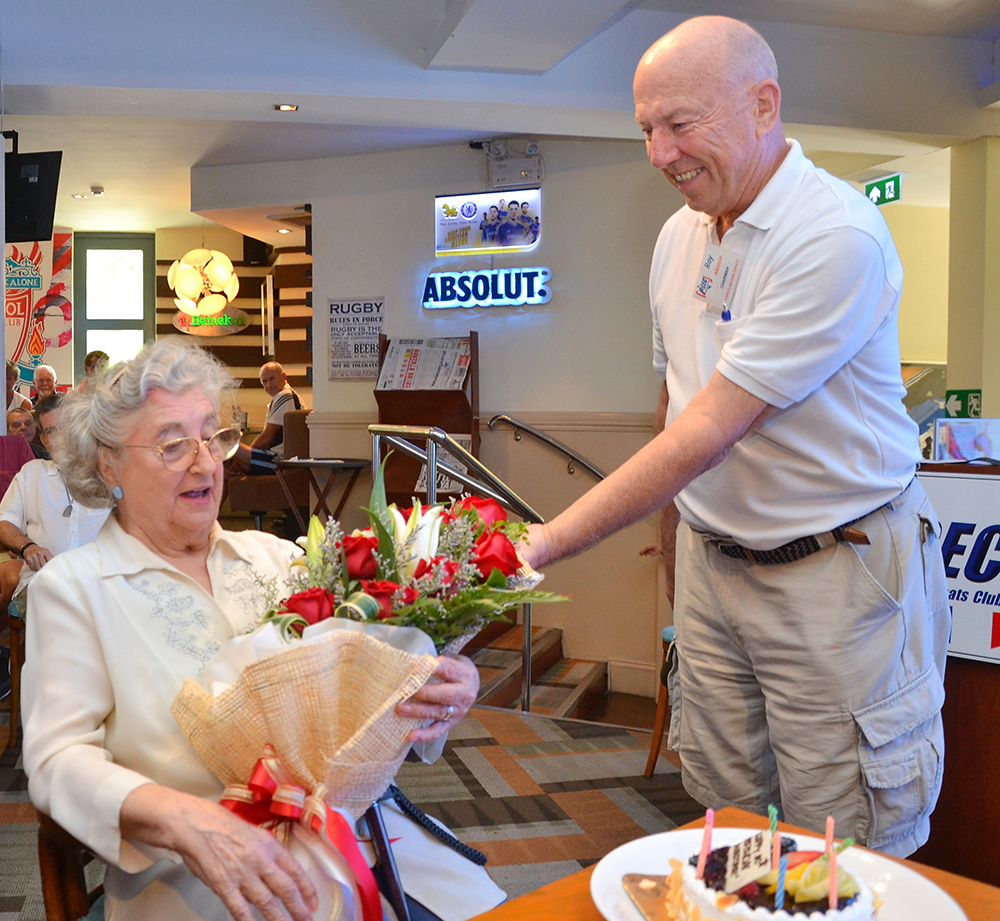 Governing Board Chairman Roy Albiston presents Marjorie Blissett with a bouquet of roses in celebration of her upcoming 90th birthday and for her continued contributions to the Pattaya City Expats Club over the years.