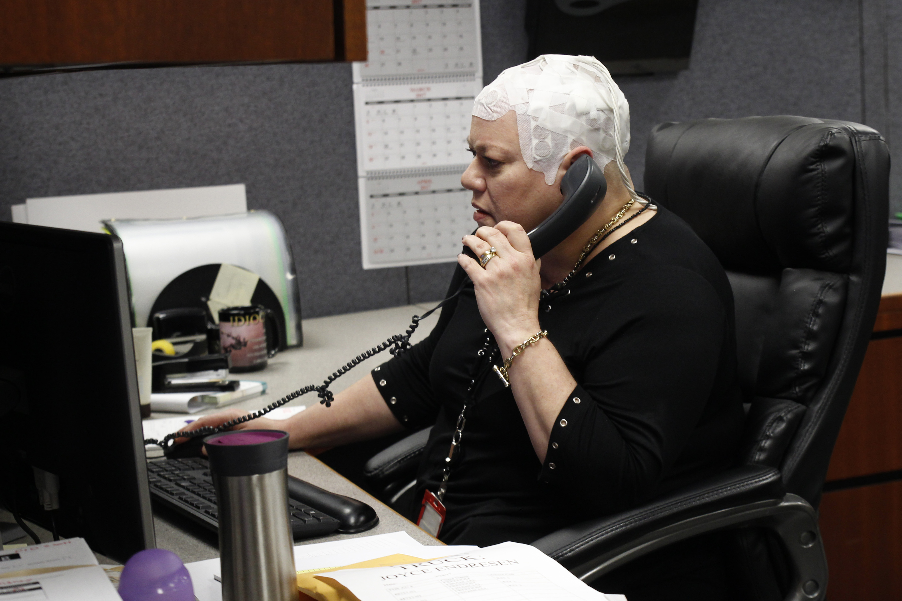 In this March 29, 2017 photo, Joyce Endresen wears an Optune therapy device for brain cancer, as she speaks on a phone at work in Aurora, Ill. (AP Photo/Carrie Antlfinger)