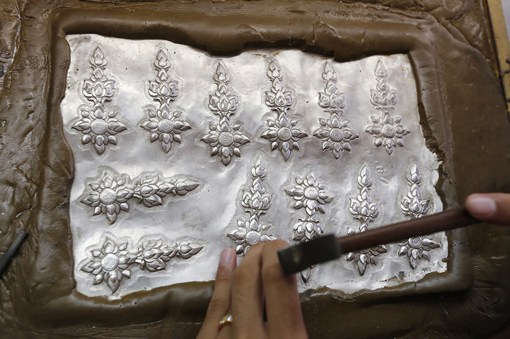 A student volunteer shapes designs on silver plates. (AP Photo/Sakchai Lalit)