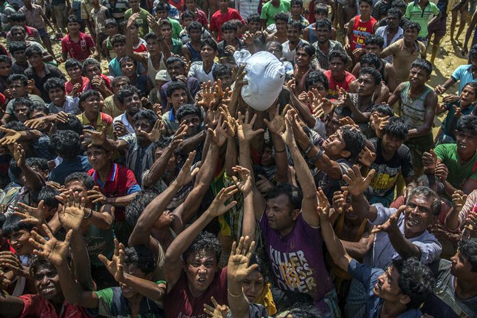 In this Thursday, Sept. 21, 2017 file photo, Rohingya Muslims, who crossed over from Myanmar into Bangladesh, stretch their arms out to catch a bag of rice thrown at them during distribution of aid near Balukhali refugee camp. With Rohingya refugees still flooding across the border from Myanmar, those packed into camps and makeshift settlements in Bangladesh are desperate for scant basic resources and fights erupt over food and water. (AP Photo/Dar Yasin, File)