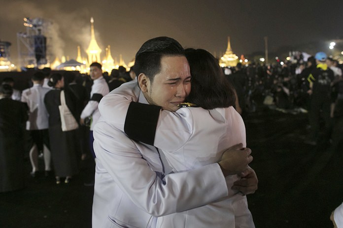 Officials hug as smoke rises from the royal crematorium of HM the late King Bhumibol Adulyadej. (AP Photo/Wason Wanichakorn)