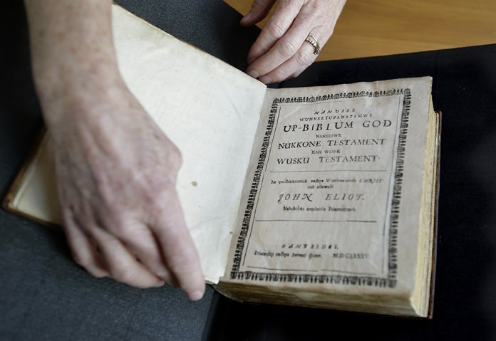 In this Thursday, Oct. 19, 2017, photo Massachusetts Institute of Technology archivist Nora Murphy places a second edition of the Eliot Indian Bible on a table at the MIT rare book collection, in Cambridge, Mass. The second edition of the Eliot Indian Bible, translated into Wampanoag, is dated 1685. Experts have relied on extensive written records in Wampanoag to reclaim the language, including 17th century phonetic translations of the King James Bible. (AP Photo/Steven Senne)
