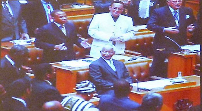 In this photo displayed during his presentation, H.E. Ambassador Geoff Doidge (white suit) stands behind a sitting Nelson Mandela during the time he was in Parliament and Nelson Mandela was President.
