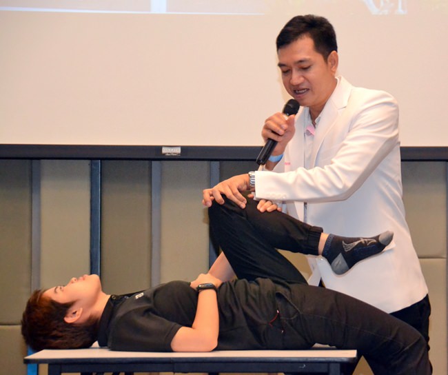 Nat with the aid of an assistant shows his audience how to perform certain exercises to treat their lower back pain.