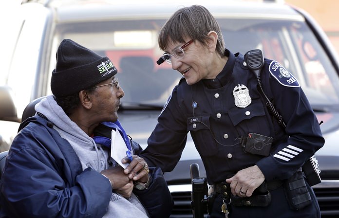 Seattle police officer Debra Pelich (right) wears a video camera on her eyeglasses as she talks with Alex Legesse before a small community gathering in Seattle. The ACLU and other organizations on Tuesday, May 22, 2018, asked Amazon to stop selling its facial-recognition tool, called Rekognition, to law enforcement agencies. (AP Photo/Elaine Thompson, File)