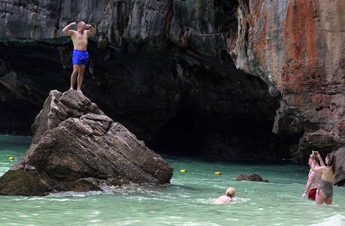Tourists pose for photos on an outcropping in Maya Bay. Thailand’s National Parks and Wildlife Department has closed the popular tourist destination to give its coral reefs and sea life a chance to recover from an onslaught that began nearly two decades ago.