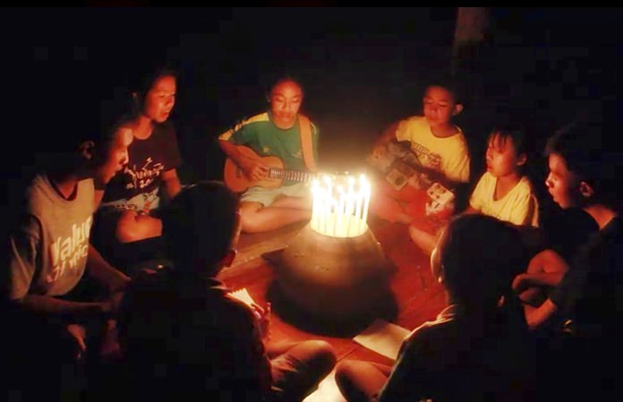 In this image from video made available on Friday, June 29, a group of young children sit around candles and play a song at a school in Buriram, eastern Thailand, in support for the missing soccer team and their coach in a flooded cave in the north. (Lek Nai Tung Kwang school via AP)