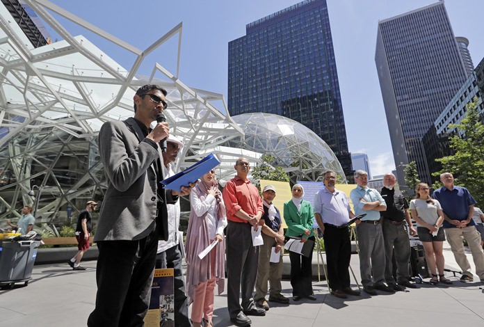 Shankar Narayan, legislative director of the ACLU of Washington, left, speaks at a news conference outside Amazon headquarters, Monday, June 18, 2018, in Seattle. Representatives of community-based organizations urged Amazon to stop selling its face surveillance system, Rekognition, to the government. They later delivered the petitions to Amazon. (AP Photo/Elaine Thompson)