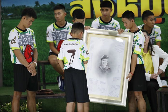 Coach Ekkapol Janthawong, left, and the 12 boys show their respect and thanks as they hold a portrait of Saman Gunan, the retired Thai SEAL diver who died during their rescue attempt. (AP Photo/Vincent Thian)