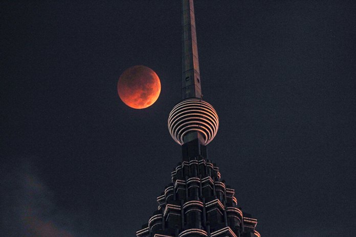 A full moon sets over the Petronas Twin Towers during a complete lunar eclipse in Kuala Lumpur, Malaysia, Saturday, July 28, 2018. (AP Photo/Yam G-Jun)
