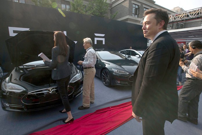 In this April 22, 2014, file photo. Tesla Motors CEO Elon Musk (right) looks on as a set of Tesla Model S sedans are delivered to customers at an event in Beijing, China. (AP Photo/Ng Han Guan)