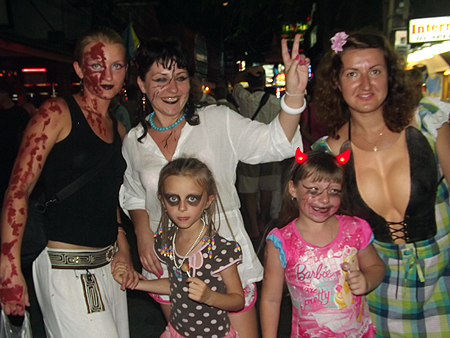 Adults dressed in their best costumes hold the hands of little ghost children.