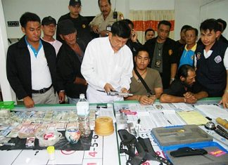 Banglamung District Chief Chawalit Saeng-Uthai inspects the confiscated handgun along with hundreds of thousands of baht, gambling slips and tables found during a raid on a Soi Buakaow home.