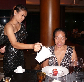 The attentive service girl pours warm red wine cherry sauce over the dessert of a dome of chocolate containing a dark cherry mousse. 