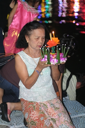 A grandmother with her family behind her prays before releasing her krathong.
