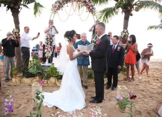 The beach of the Pinnacle Resort provides a picturesque romantic backdrop as Father Fred Doell conducts the wedding ceremony.