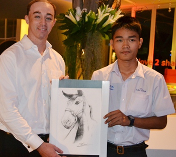 Young artist Weerapat Maettaneesakhudee (right), shown here presenting one of his paintings to high bidder, Nova Platinum Hotel General Manager David Leslie Roberts, produced more than half the canvases which were auctioned. 
