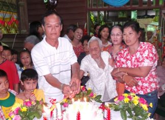 Friends and family help Rhan Lonlua light the candles on her 100th birthday cake.