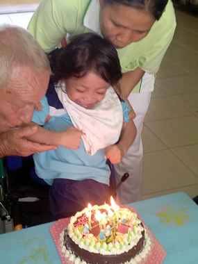 Bernie and a care-giver help Fahsai blow out the candles on her birthday cake.