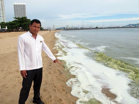 A local hotel employee points out the green slick that washed up on a Sattahip Beach.