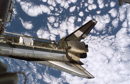 Backdropped by a cloud-covered Earth, Space Shuttle Discovery is featured in this image while docked with the International Space Station.