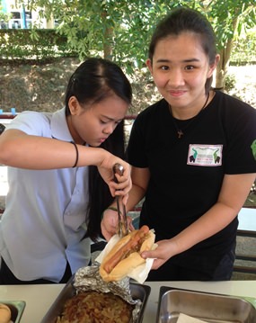 IB student Sofia gets help preparing the hot dogs.