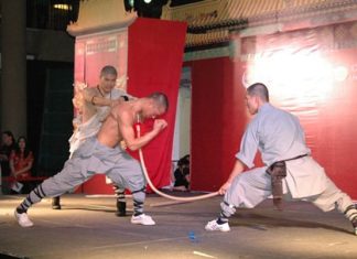 A Shaolin member uses his neck to push against a sharp spear while another Shaolin member hits his back with a wooden stick.