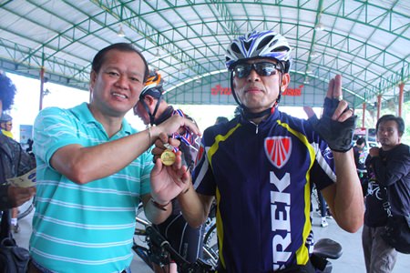Detchana Bunyapraphachot (left), manager of Banglamung Cable TV, presents a medal to one of the first 300 bicyclists to finish the 40 km race,