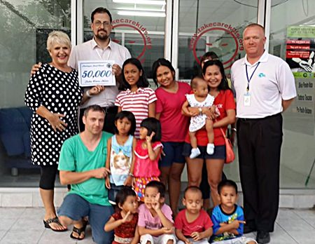 Eva Johnson (left) and Earl Brown (right) present a cheque for 50,000 baht to the children and organizers of the Take Care Kids charity.