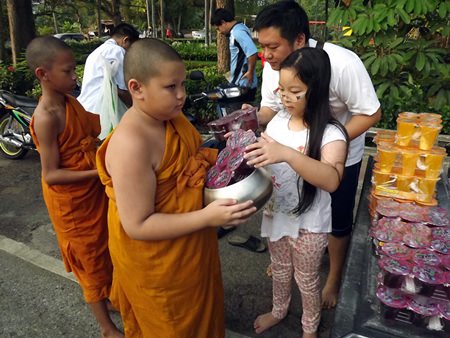 A father leads his daughter to offer alms.