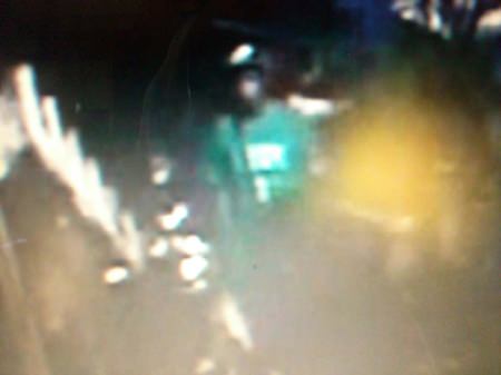 This blurry image, taken from security camera footage, shows a thin young man in a green shirt steeling a motorcycle.