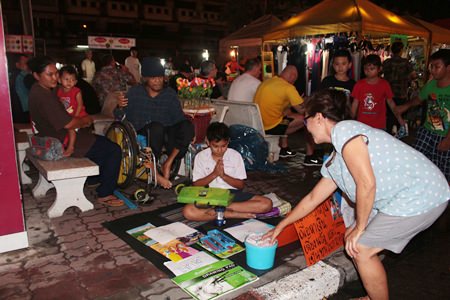 Eakmongkol “Nong Miw” Samerpark, with his family in the background, sells a drawing and receives a donation at the Thepprasit second-hand market.
