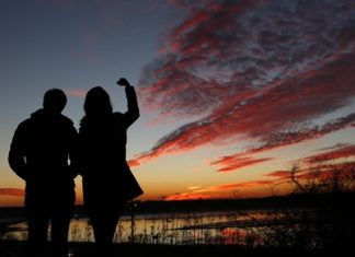 Kathleen O’Brien, of Portland, Maine, and Kathryn McBrady, of Scarborough, Maine, take in the view of a fiery winter sunset overlooking Back Cove, Thursday, Jan. 7, 2016, in Portland, Maine. Get ready for weather whiplash as powerful climatic forces elbow each other for starring roles in a weird winter show. (AP Photo/Robert F. Bukaty)