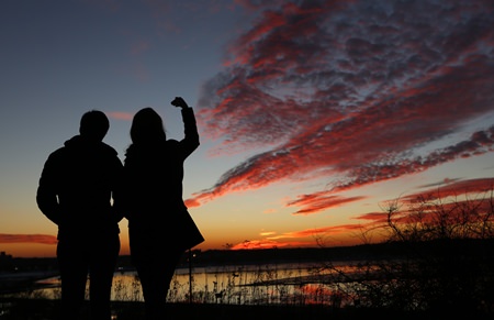 Kathleen O’Brien, of Portland, Maine, and Kathryn McBrady, of Scarborough, Maine, take in the view of a fiery winter sunset overlooking Back Cove, Thursday, Jan. 7, 2016, in Portland, Maine. Get ready for weather whiplash as powerful climatic forces elbow each other for starring roles in a weird winter show. (AP Photo/Robert F. Bukaty)