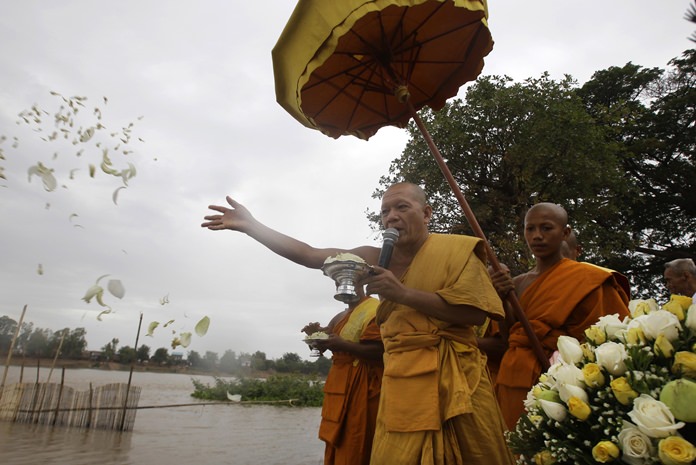 A monk casts flowers onto the Tonle Sap river during a Buddhist ceremony as locals search for missing Buddha statues at Kean Kleang village, Kampong Chhnang province, northwest of Phnom Penh, Cambodia, Thursday, Aug. 18. (AP Photo/Heng Sinith)